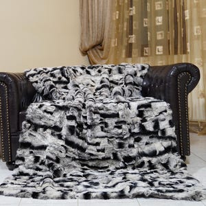 May include: A black and white faux fur throw blanket draped over a dark brown leather armchair. The blanket has a zebra stripe pattern. A fireplace with a burning fire is in the background.