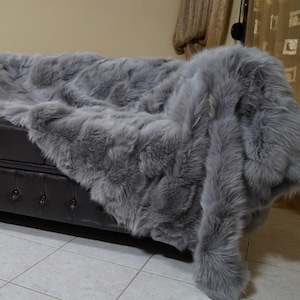 May include: A dark brown leather sofa with a gray faux fur throw draped over it. The sofa has button tufting and nailhead trim. The throw is a soft, fluffy material.