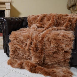 May include: A brown, fluffy throw blanket draped over a dark brown leather armchair. The blanket has a shaggy texture and appears soft. The armchair is in front of a fireplace.