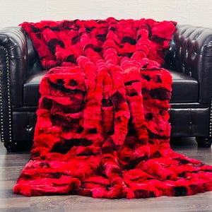 May include: A plush red and black faux fur throw blanket draped over a black leather armchair. A wooden acoustic guitar leans against the wall to the left of the chair. The blanket has a textured, patterned design.