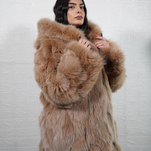 May include: A luxurious, full-length coat in a warm, light brown hue. The coat features a large, fluffy hood and sleeves, creating a voluminous silhouette. The fur appears soft and dense, suggesting a high-quality material. The coat is a statement piece.