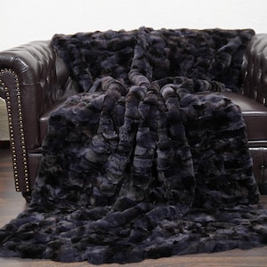 May include: A dark gray faux fur throw blanket draped over a brown leather armchair. The blanket has a textured, plush appearance. A wooden acoustic guitar leans against the wall to the left of the chair.