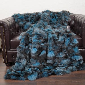May include: A luxurious faux fur throw blanket in shades of teal and charcoal gray draped over a dark brown leather armchair. A wooden acoustic guitar leans against the wall, adding a touch of musical charm.