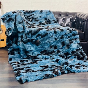 May include: A plush, faux fur throw blanket in shades of teal and black drapes over a black leather sofa. A wooden acoustic guitar leans against the wall, adding a touch of musical charm to the scene.