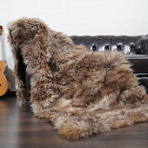 May include: A brown and tan faux fur throw draped over a dark brown leather Chesterfield sofa. A wooden acoustic guitar leans against a white wall, adding a touch of rustic charm to the scene.