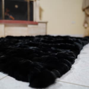 May include: A large, black fur rug with a plush texture. The rug is rectangular and covers a significant portion of the floor. The fur appears dense and soft, creating a luxurious aesthetic. The rug is placed on a tiled floor.