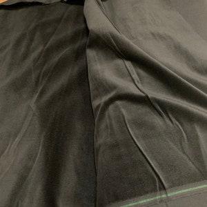May include: A close-up of black velvet fabric, folded and draped. The fabric has a soft, plush texture and a deep, rich color. The edges of the fabric are visible, showing the cut and the backing. The fabric is likely used for clothing or home decor.
