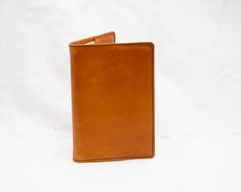 Puede incluir: Una cubierta de cuaderno de cuero marrón con un diseño sencillo.