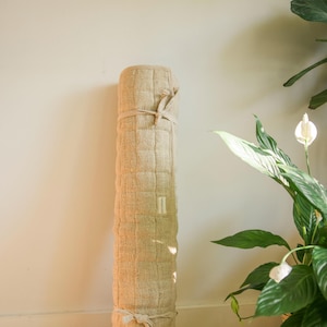 Eco-friendly natural hemp yoga mat rolled and leaning stylishly against a wall near a houseplant. Perfect for sustainable yoga, meditation, or mindful living spaces.