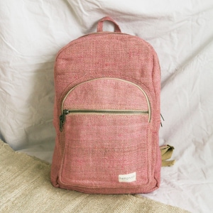 May include: A pink hemp backpack with a zipped front pocket and the word "hempwh" printed on the bottom.
