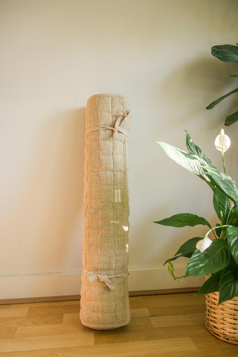 Eco-friendly natural hemp yoga mat rolled and leaning stylishly against a wall near a houseplant. Perfect for sustainable yoga, meditation, or mindful living spaces.