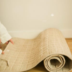 Person gently unrolling sustainable hemp yoga mat on indoor wood floor, highlighting its soft, breathable fabric