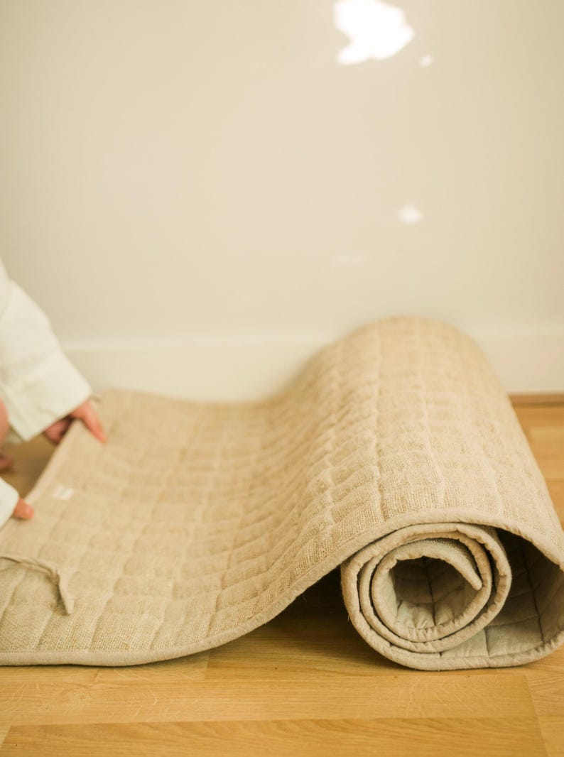 Person gently unrolling sustainable hemp yoga mat on indoor wood floor, highlighting its soft, breathable fabric