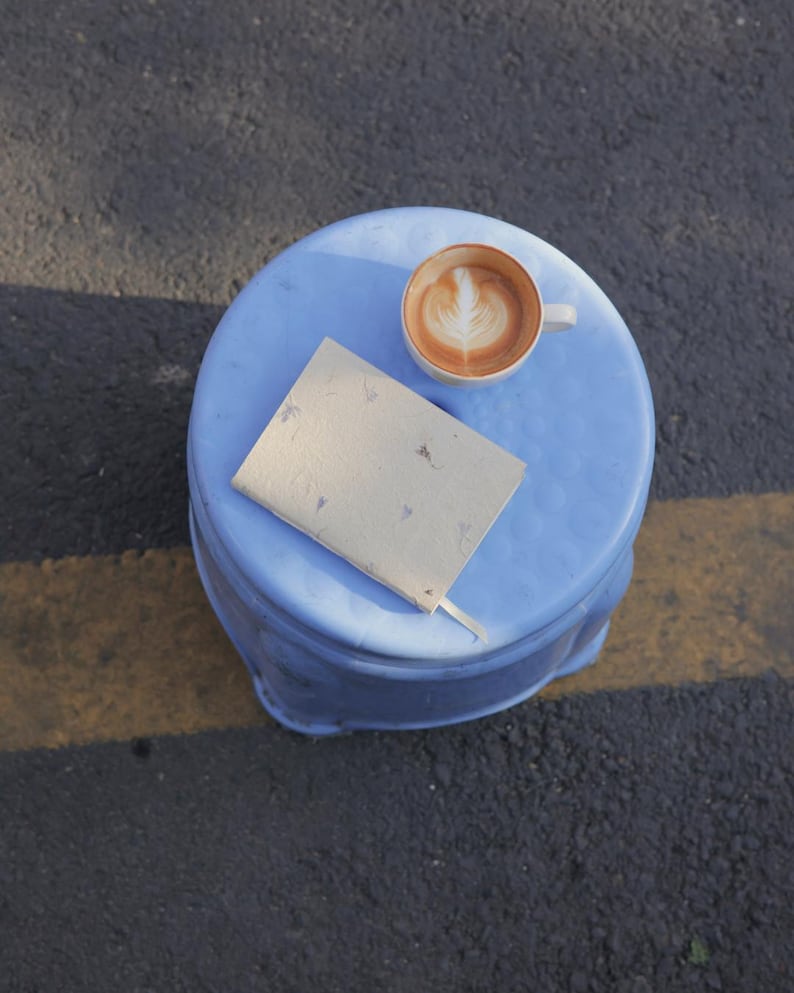 A handmade paper notebook placed on a small blue table next to a coffee cup, capturing a moment of calm creativity. This image evokes the use of the notebook as a daily journal, mindful writing notebook, or eco friendly sketchbook