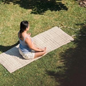 Woman meditating outdoors on a natural hemp yoga mat under sunlight, promoting slow living, mental wellness, and sustainable yoga practice with biodegradable, non-toxic materials