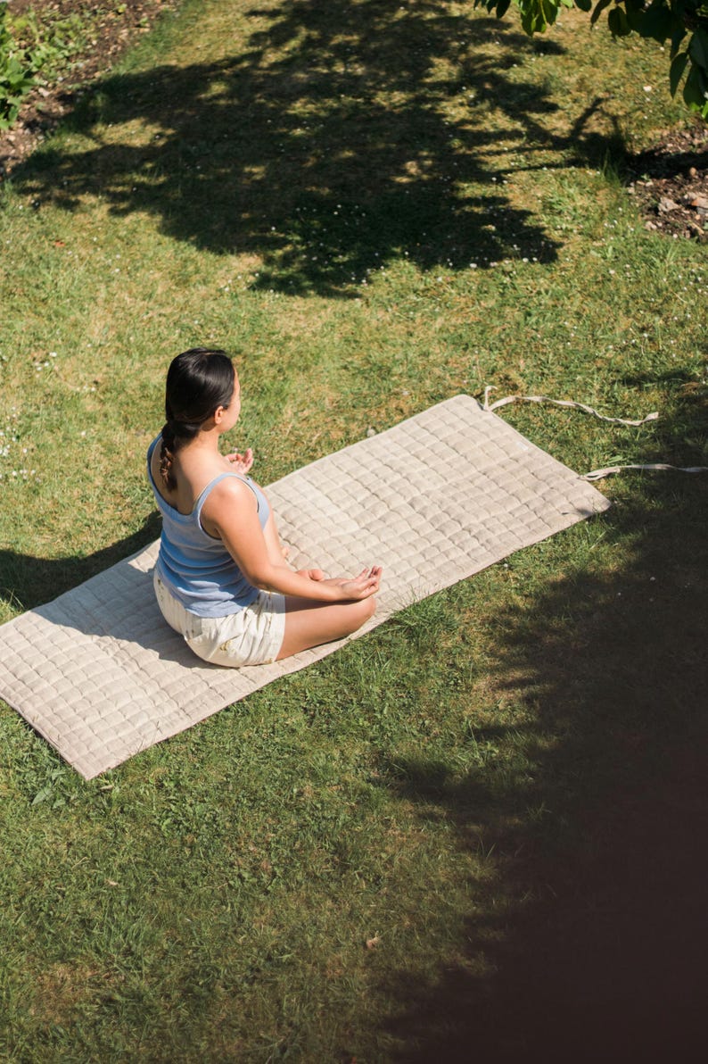 Woman meditating outdoors on a natural hemp yoga mat under sunlight, promoting slow living, mental wellness, and sustainable yoga practice with biodegradable, non-toxic materials