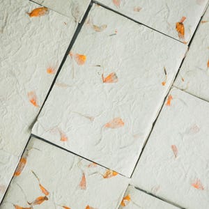 A composition of many recycled paper notebooks featuring warm-toned floral inclusions. The layout displays color variation and texture across the collection, showcasing eco friendly notebook sets and handmade stationery bundles.