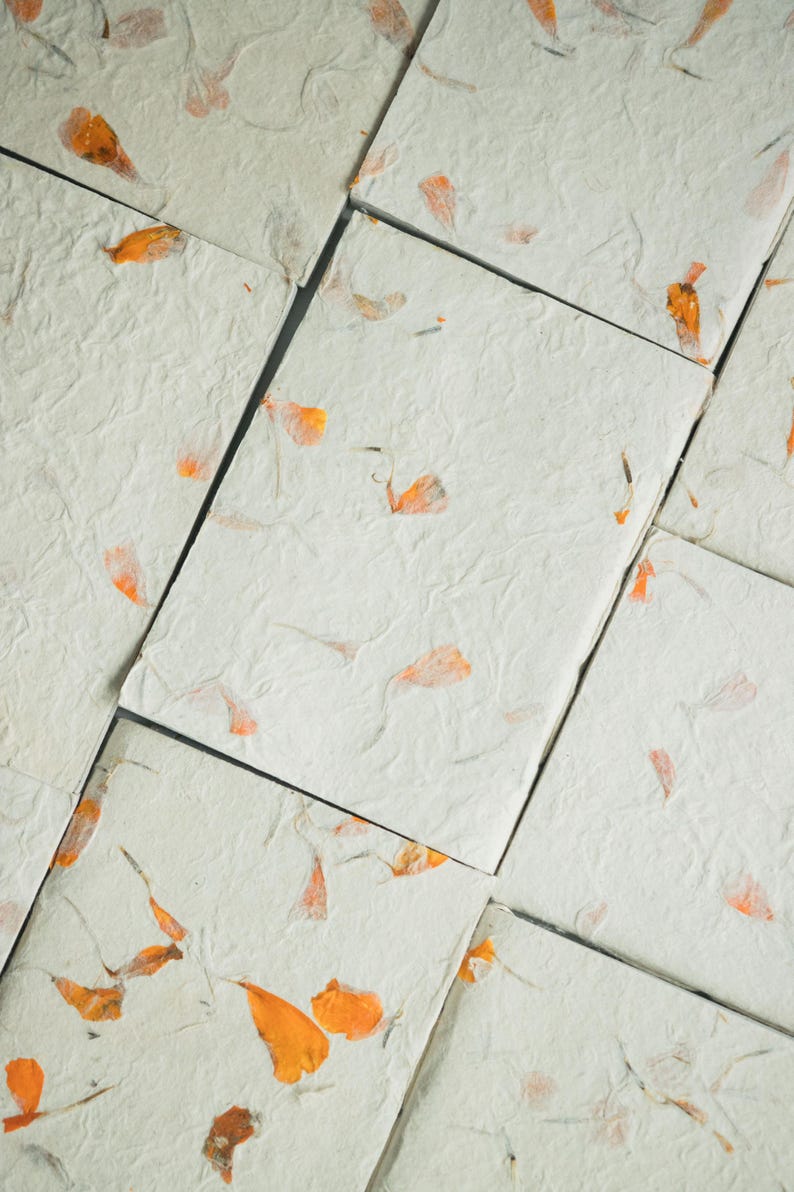 A composition of many recycled paper notebooks featuring warm-toned floral inclusions. The layout displays color variation and texture across the collection, showcasing eco friendly notebook sets and handmade stationery bundles.