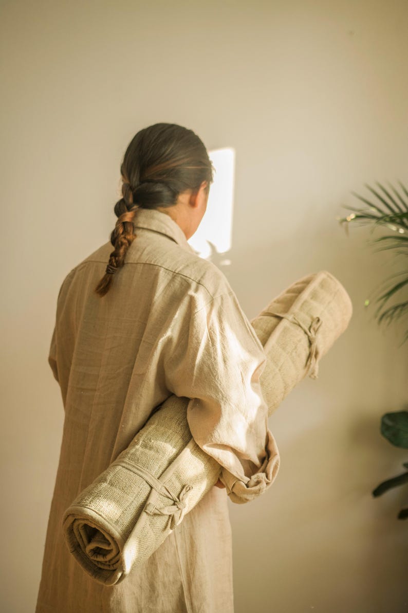 Back view of person carrying rolled hemp yoga mat using natural fiber shoulder strap. Great for on-the-go yoga and eco-travel