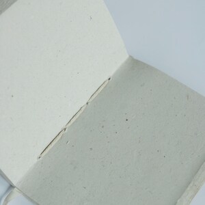An open lokta paper journal showing the soft, textured inner pages made from natural fibers. The blank pages emphasize its use as a handmade sketchbook, writing notebook, or sustainable art journal.
