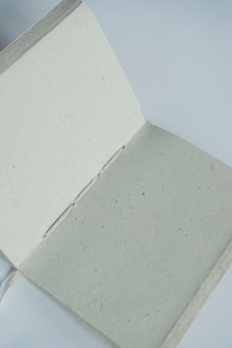 An open lokta paper journal showing the soft, textured inner pages made from natural fibers. The blank pages emphasize its use as a handmade sketchbook, writing notebook, or sustainable art journal.