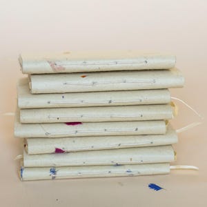 A stack of several handmade paper journals placed one on top of another. The edges show subtle differences in thickness, natural fibers, and petal inclusions. Strong visual for eco friendly stationery, artisanal notebooks, and recycled paper gifts.