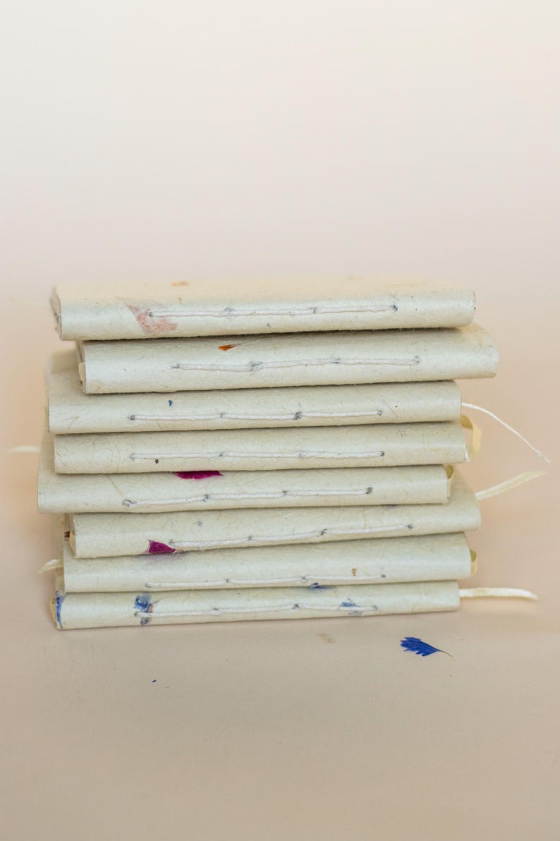 A stack of several handmade paper journals placed one on top of another. The edges show subtle differences in thickness, natural fibers, and petal inclusions. Strong visual for eco friendly stationery, artisanal notebooks, and recycled paper gifts.