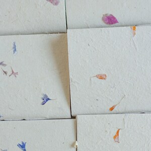 A detailed arrangement of multiple handmade paper notebook covers, each with subtle petal and leaf inclusions. The textured surfaces highlight the natural fibers typical of lokta journals, eco friendly stationery, and artisan paper products.