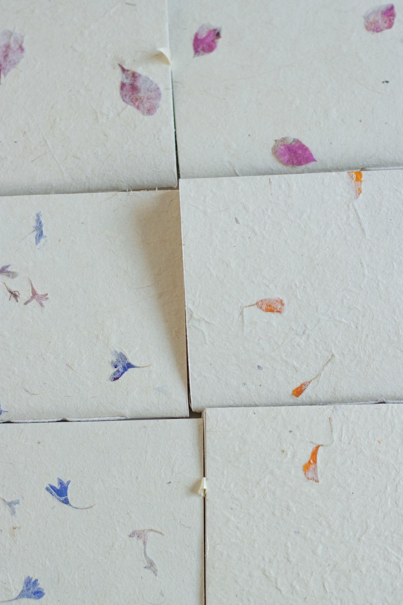 A detailed arrangement of multiple handmade paper notebook covers, each with subtle petal and leaf inclusions. The textured surfaces highlight the natural fibers typical of lokta journals, eco friendly stationery, and artisan paper products.