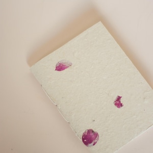 A notebook with pressed bougainvillea flowers on its cover placed on a soft blush-colored surface. The gentle tones emphasize the calming, natural feel of this eco friendly handmade notebook, suitable as a botanical diary or nature-inspired stationery piece.