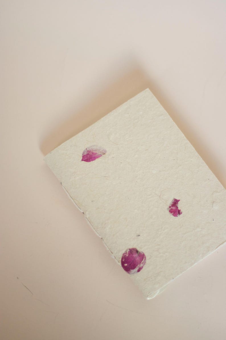 A notebook with pressed bougainvillea flowers on its cover placed on a soft blush-colored surface. The gentle tones emphasize the calming, natural feel of this eco friendly handmade notebook, suitable as a botanical diary or nature-inspired stationery piece.