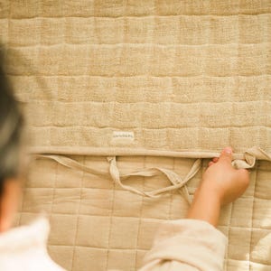 Close-up of hand folding a quilted hemp yoga mat to show texture, stitching, and craftsmanship. Handmade from sustainable plant fibers—non-toxic, plastic-free, and compostable.
