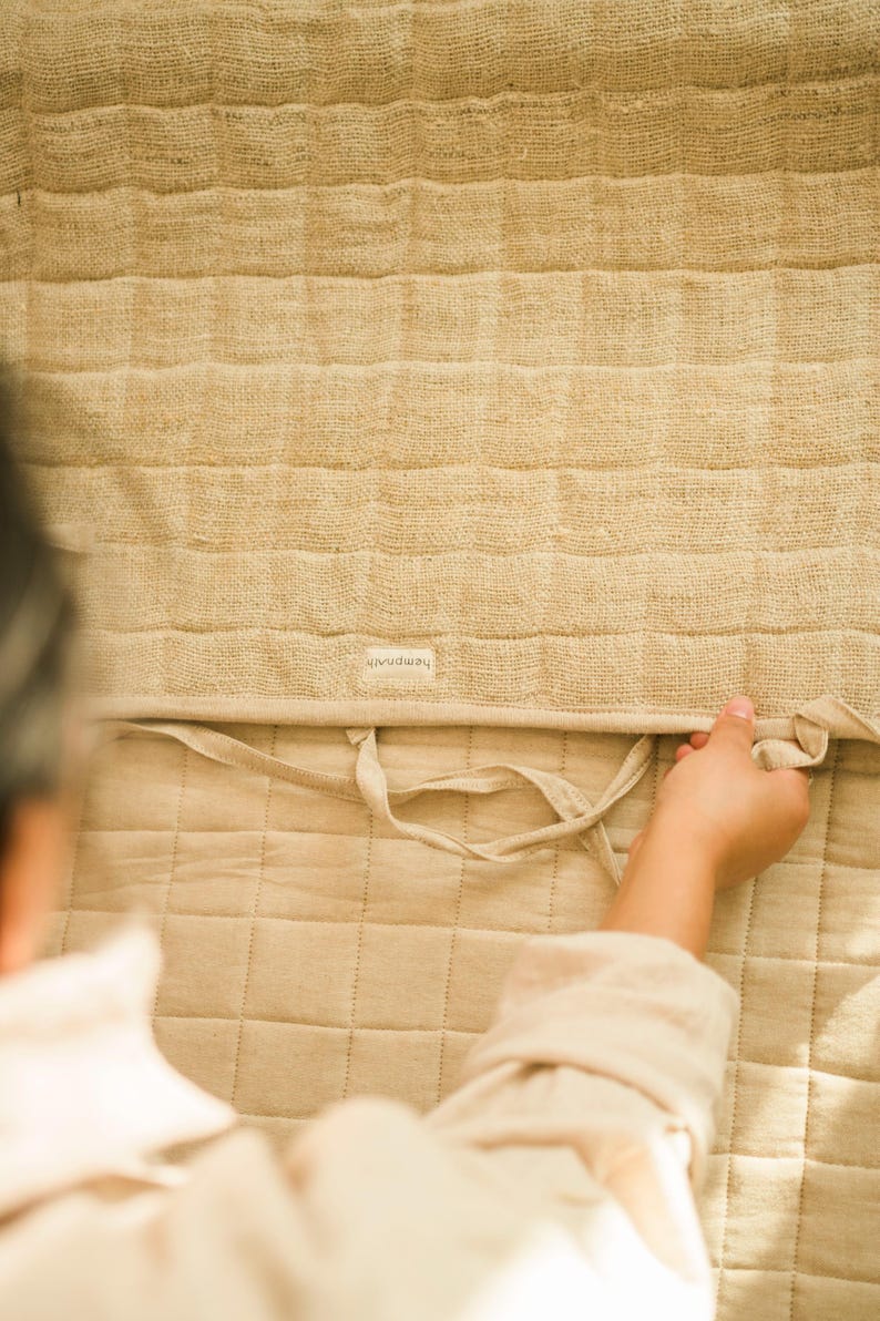 Close-up of hand folding a quilted hemp yoga mat to show texture, stitching, and craftsmanship. Handmade from sustainable plant fibers—non-toxic, plastic-free, and compostable.