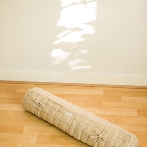 Rolled eco-friendly yoga mat made from 100% natural hemp lying on hardwood floor, bathed in warm sunlight. Designed for minimalists and earth-conscious practitioners