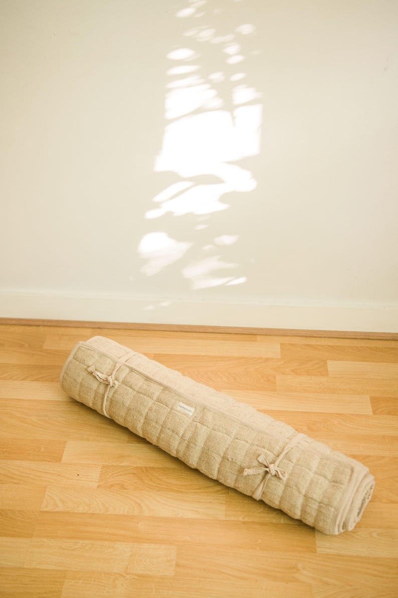 Rolled eco-friendly yoga mat made from 100% natural hemp lying on hardwood floor, bathed in warm sunlight. Designed for minimalists and earth-conscious practitioners