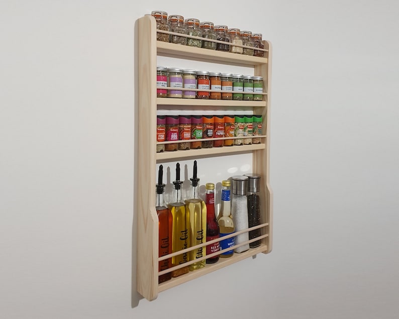 May include: A wooden spice rack with four shelves, holding various glass jars of spices and bottles of oil and vinegar. The rack is mounted on a white wall.
