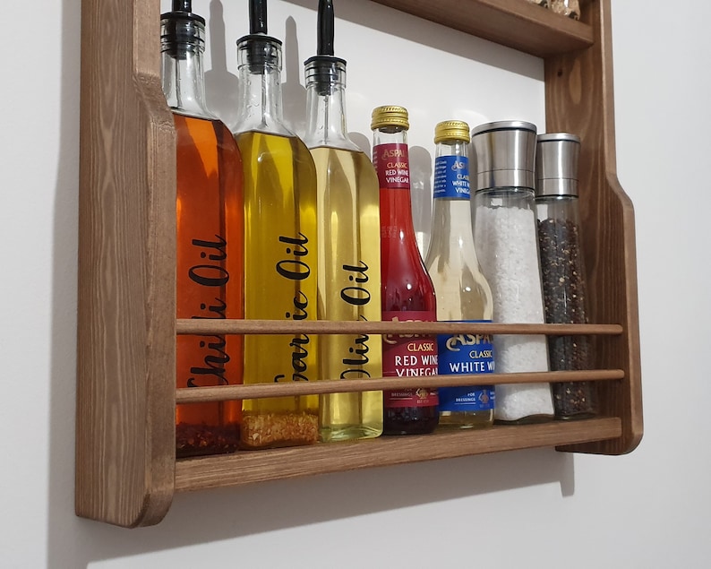 May include: Wooden wall-mounted shelf with six glass bottles and two glass shakers. The bottles contain various liquids, including chili oil, garlic oil, olive oil, red wine vinegar, and white wine vinegar. The shakers contain salt and pepper.