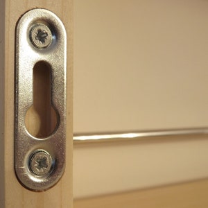 May include: A silver metal hanging hook with two screws attached to a wooden surface. The hook has a keyhole-shaped opening.