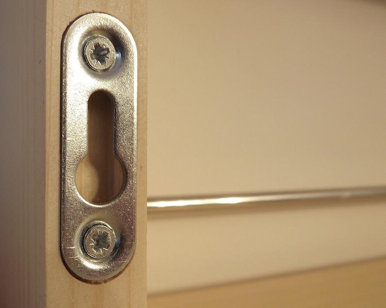 May include: A silver metal hanging hook with two screws attached to a wooden surface. The hook has a keyhole-shaped opening.