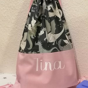 Könnte beinhalten: Eine rosa Kordeltasche mit einem schwarzen und weißen Drachenmuster. Die Tasche hat einen rosa Boden mit dem Namen "Tina" in weiß.