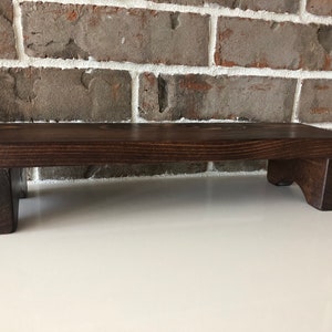 May include: A dark brown wooden riser with a rectangular top and two short legs on each side. The riser is made of solid wood and has a natural wood grain.