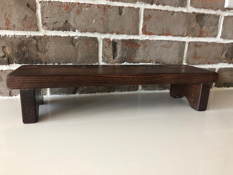 May include: A dark brown wooden riser with a rectangular top and two short legs on each side. The riser is made of solid wood and has a natural wood grain.