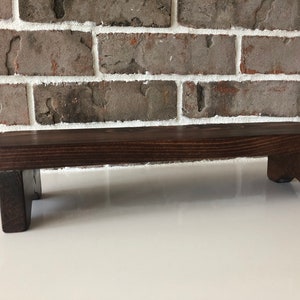May include: A dark brown wooden shelf with two small legs on each side. The shelf is made of natural wood and has a rustic look.