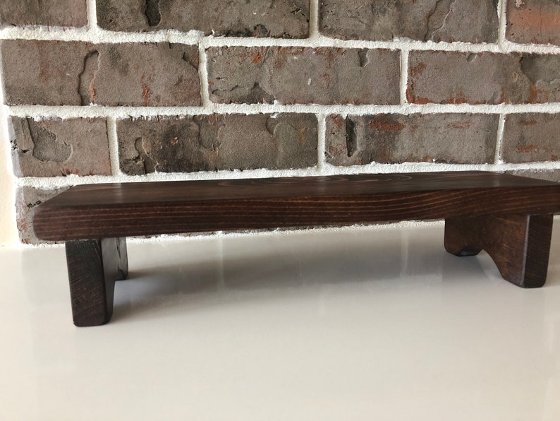 May include: A dark brown wooden shelf with two small legs on each side. The shelf is made of natural wood and has a rustic look.