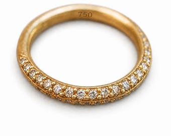 May include: A gold band ring featuring a row of small, round, clear stones set along the outer edge. The interior of the band is clearly stamped with the number 750, indicating the gold purity. The metal has a warm, polished yellow gold finish.
