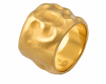 Puede incluir: Un anillo ancho de oro con una superficie texturizada, orgánica y ondulada. El interior de la banda presenta un acabado pulido y está marcado con el texto 750 y un símbolo G dentro de un borde circular decorativo.