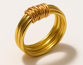 May include: A gold-toned ring featuring a multi-strand band design. The ring is composed of several parallel circular wires that are held together at the top by a series of tightly wrapped, smaller gold-toned wire coils, creating a layered look.