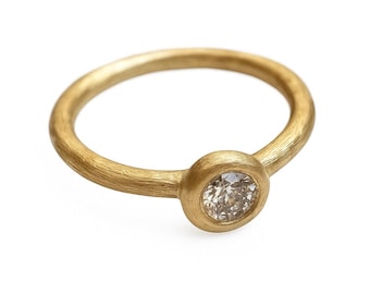 May include: A gold ring with a round band and a bezel-set, round-cut diamond. The ring has a textured finish and a warm, yellow hue. The diamond appears to be a light champagne color.