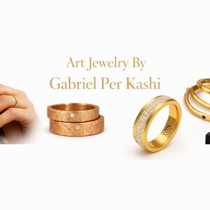 May include: An assortment of gold jewelry, including rings and bangles. One ring is encrusted with small diamonds. The image also features a hand wearing a delicate gold ring and a stack of gold rings. The brand name "Art Jewelry By Gabriel Per Kashi" is displayed.