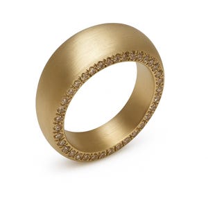 May include: A gold-colored ring with a brushed finish. The ring has a thick band and is lined with small, light brown gemstones. The ring is set against a white background.